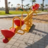 لعبة توازن الميزان الرباعي في حديقة، مصنوعة من هيكل معدني متين ومقاعد بلاستيكية ملونة، مصممة لتتسع لأربعة أطفال.