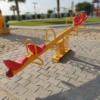 لعبة توازن الميزان الرباعي في حديقة، مصنوعة من هيكل معدني متين ومقاعد بلاستيكية ملونة، مصممة لتتسع لأربعة أطفال.